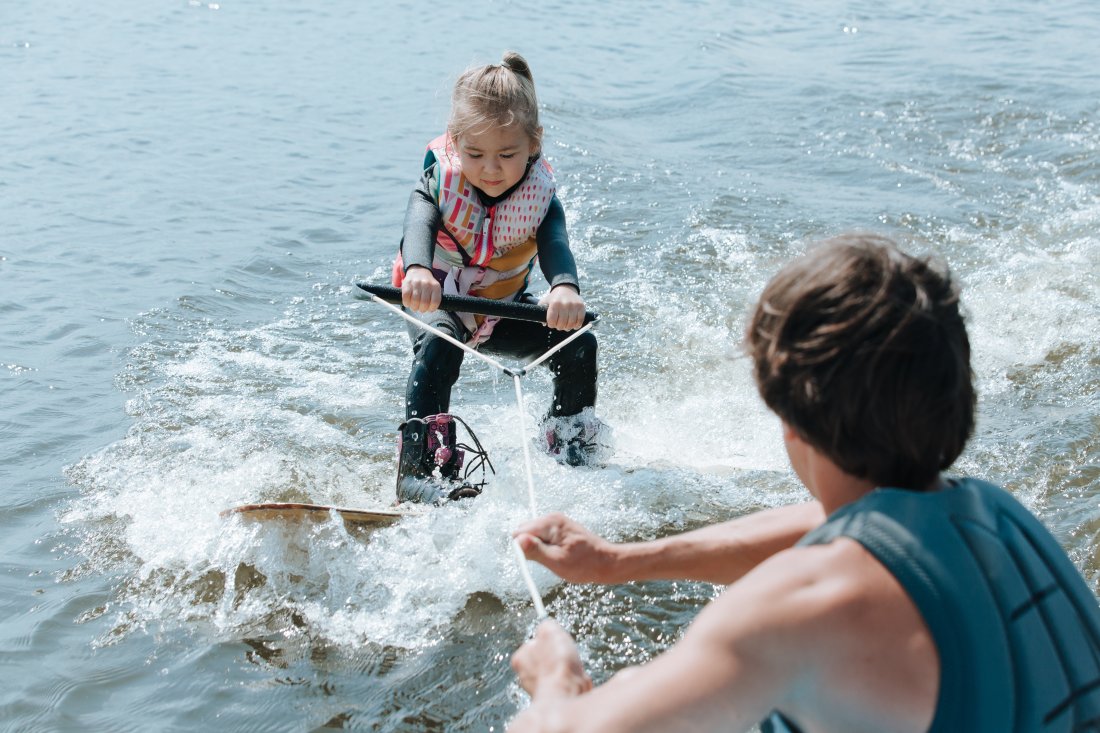 Mand hjælper en lille pige med at stå på wakeboard.
